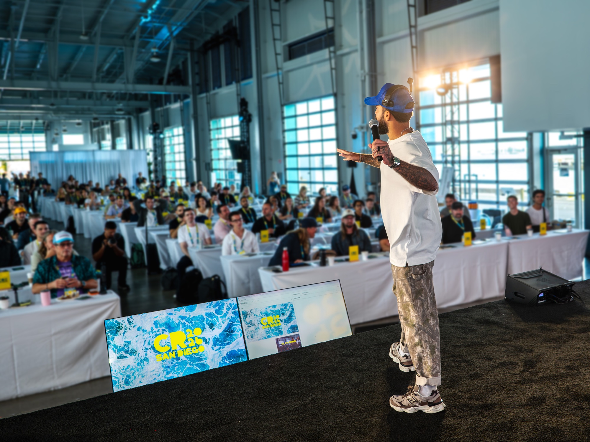 A speaker addressing a full room of attendees, with afternoon sunlight across the San Diego venue